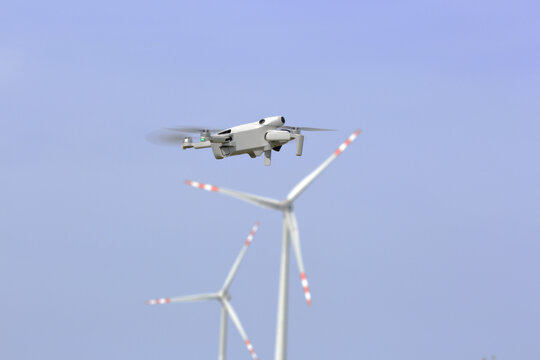Dron w powietrzu, w tle turbiny wiatrowe.