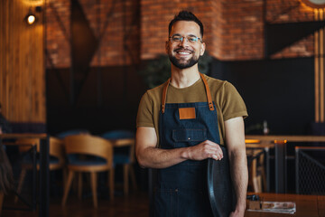 Happy confident young waiter entrepreneur looking at camera, smiling male small cafe business owner employee standing in restaurant, millennial businessman wear apron posing in coffee shop - 789034535