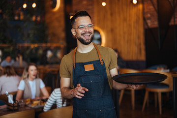 Happy confident young waiter entrepreneur looking at camera, smiling male small cafe business owner employee standing in restaurant, millennial businessman  - Powered by Adobe