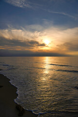 Sunset, illuminated sea. Sandy beach in the foreground. Light waves. Baltic Sea