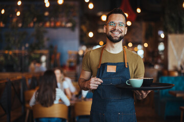 Happy confident young waiter entrepreneur looking at camera, smiling male small cafe business owner employee standing in restaurant, millennial businessman wear apron posing in coffee shop - 789035760