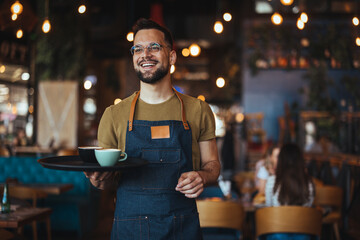 Waist up portrait of handsome waiter smiling cheerfully at camera standing in restaurant or cafe, copy space. Young waiter serving coffee in a cafe and looking at camera. - 789036569