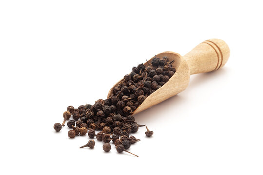 Front view of a wooden scoop filled with Organic Sheetal Chini (Piper cubeba) seeds. Isolated on a white background.