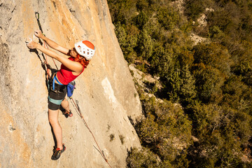 A woman is climbing a rock wall with a red helmet on - obrazy, fototapety, plakaty