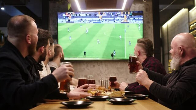 Group of friends clinking beers in a modern sports bar. Leisure and entertainment concept.