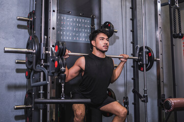 Dedicated and focused young male athlete doing back squats on a smith machine in a well-equipped gym, showing strength and concentration.