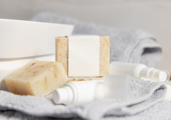 Soap bar with blank label near basin, towel and cream bottles in bath, mockup