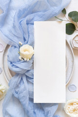 Card near blue tulle fabric knot and cream roses on plates top view copy space, wedding mockup