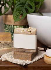 Soap bar with blank label on bath wooden countertop near monstera plant close up, mockup