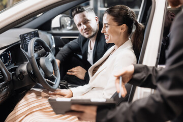 Happy family of a woman and a man in a modern electric car showroom. The family is going to buy or rent a new car. Family purchase, hire purchase and sale.