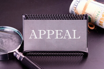 Word APPEAL on the business card next to a roll of money and a magnifying glass on a black...