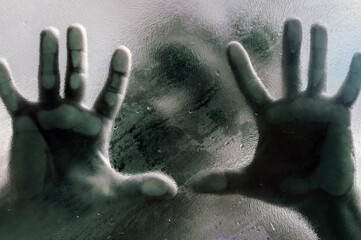 Mans figure with hands pressed against frosted glass. Shadow of a man behind the matte glass blurry hand and body soft focus.