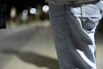 Male legs in jeans against the background of a night park in the light of lanterns. A man stands in a park in the summer at night, illuminated by night lanterns.