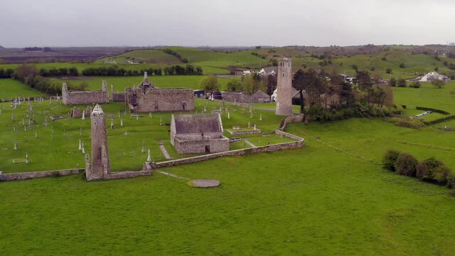 Dynamic aerial shot approaches old round towers and buildings at Clonmacnoise