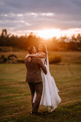 Valmiera, Latvia- July 28, 2023 - A bride and groom in a sunset embrace, with the groom's back to...