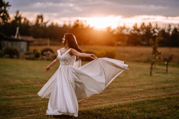 Fototapeta na wymiar Valmiera, Latvia- July 28, 2023 - A joyful bride twirling in her wedding dress outdoors with a sunset backdrop.