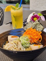 Beautiful Colorful Miso Soup in a Black Bowl with Tropical Drink and flowers in the Backround.