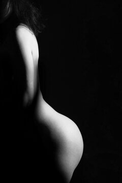 Nude, erotic concept. Woman posing naked in studio. Model standing in shadow. Girls naked body silhouette illuminated with light. Image contains noise and motion blur. Black and white image