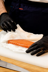 close-up of a chef's hands in black gloves dipping salmon fillet with a napkin