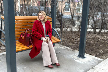 Urban loneliness: full woman in red coat and with coffee in hand on city swing in sad reverie