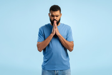 African American man with clasped hands praying over blue background. Advertisement concept