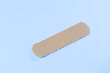 A bandage is laying on a blue surface. The bandage is tan and is not in use