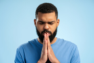 Close up portrait of African American man praying over blue background. Advertisement concept