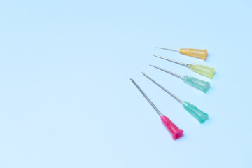 A row of five different colored plastic needles are on a blue background. The needles are of...