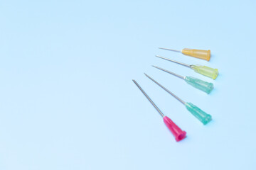 A row of five different colored plastic needles are on a blue background. The needles are of different sizes and colors, with one being green and the others being red, yellow, and blue