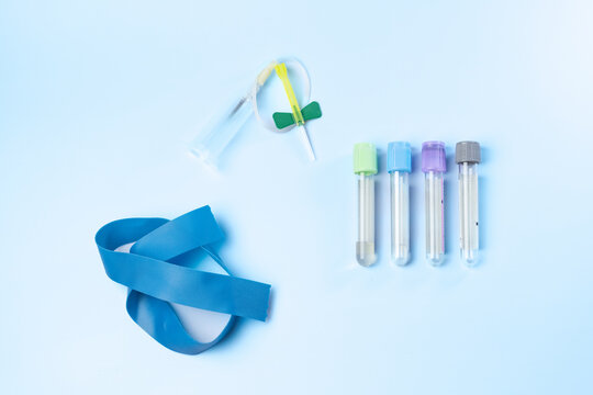 A blue ribbon is next to a syringe and four vials. The ribbon is blue and white and has a pattern. The vials are all different colors and are placed on a blue surface