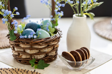 Turquoise and blue Easter eggs in a brown basket on the table. Blue gypsophila flowers in a vase...