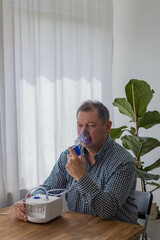 Elderly man sitting on a table and using a nebulizer mist at home