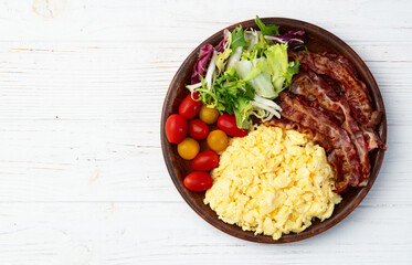 Breakfast plate . Scrambled eggs , bacon , cherry tomatoes and salad