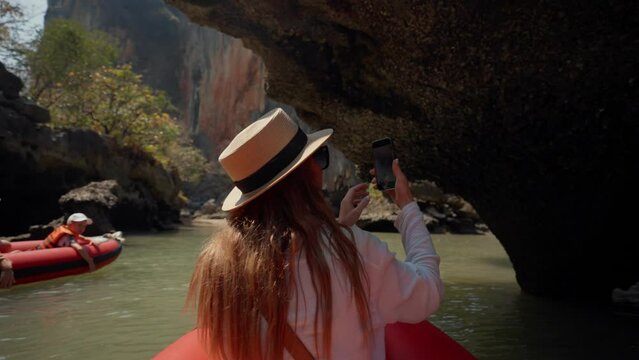 Woman sitting on boat passing lagoon. Back view female travel, riding on gondola, sitting on ship bow and looking take a photo of nature in a wicker hat in summer day. Tourism, expression lifestyle.