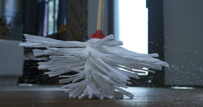 Super slow motion of spinning wet mop with splashing water drops is being turned by house wife or maid during floor domestic home cleaning at 1000 fps. Household equipment, industrial cleaning service