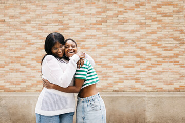 Portrait of two young cheerful black women embracing and smiling cheerfully in an outdoor setting.