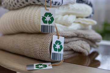 Beautifully folded woolen clothing with a recycling label lies on the table. Knitted sweaters in delicate colors with a recycling label. Eco-friendly items, biodegradable clothing, recycling.