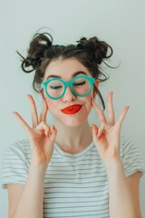 A cheerful young woman wearing large teal glasses and red lipstick flashing the peace sign with both hands.