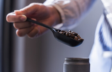 Close up barista holding black roasted coffee in spoon preparing to make coffee in shop