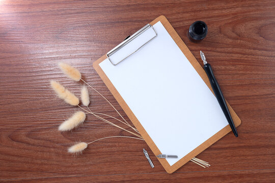 Blank clipboard with dip pen on wooden texture background. Writer workplace concept.