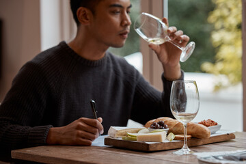 Drinking, eating and restaurant with asian man food critic writing notes for review as customer. Cheese platter, glass and wine with consumer person in eatery for gourmet cuisine or meal assessment - obrazy, fototapety, plakaty