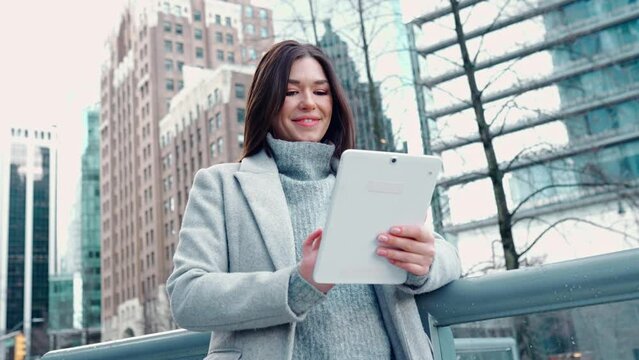 Young happy busy business woman professional leader or female student standing on big city street using digital tablet fintech pad device technology looking at pad thinking of financial success.