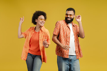 Happy African American couple in stylish eyeglasses dancing while posing in studio