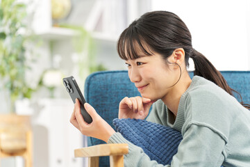 ソファで寝転んでスマートフォンを見る女性