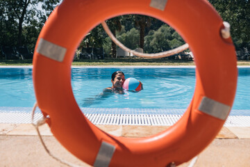 Girl playing with a ball in the pool seen behind the lifesaver ring