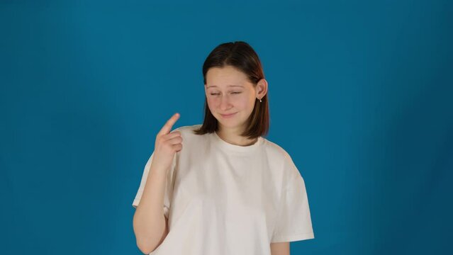 Young woman shakes index finger expressing dissent. Lady in t-shirt makes gestures indicating clear refusal on blue background