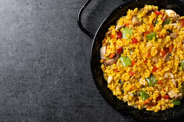 Yellow rice with chicken and vegetables on black slate background. Top view. Copy space