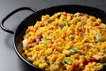 Yellow rice with chicken and vegetables on black slate background. Close up