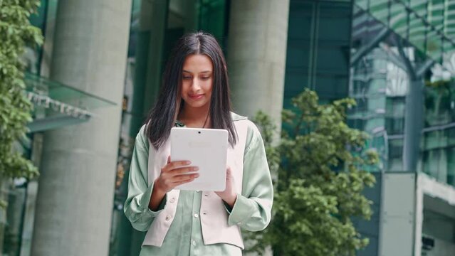 Young busy happy Indian business woman professional or female student standing on big city urban street using digital tablet fintech pad device technology connected for work and communication.