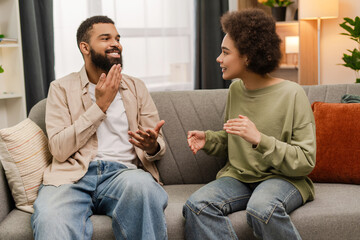 Positive young African American couple looking at each other, communicate in sign language